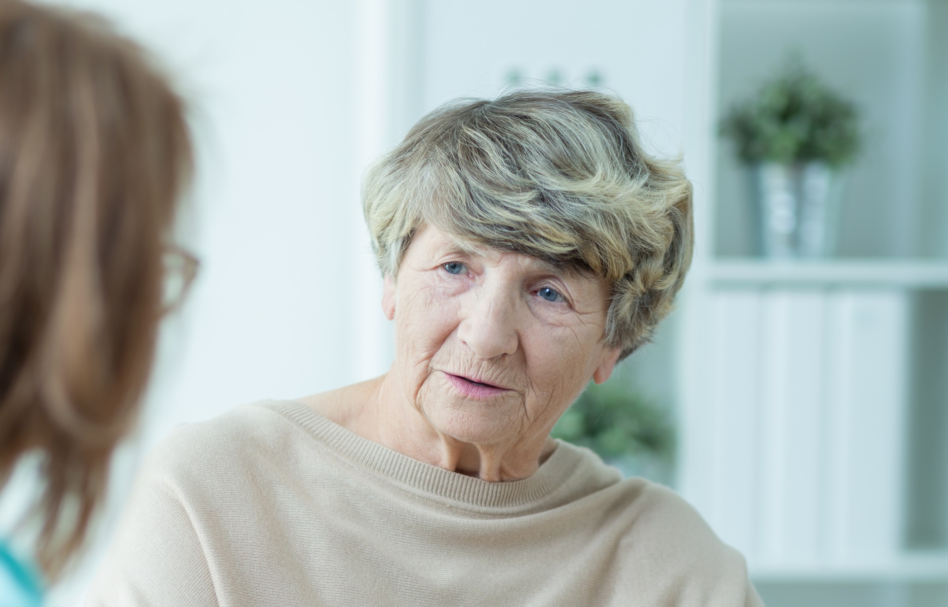 An elderly woman engaged in serious conversation with a female healthcare provider inside a home setting. 